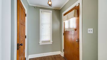 Un couloir avec des portes en bois, une fenêtre avec des stores et un luminaire au plafond.