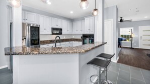 A modern kitchen with white cabinets, granite countertops, stainless steel appliances, and pendant lighting.