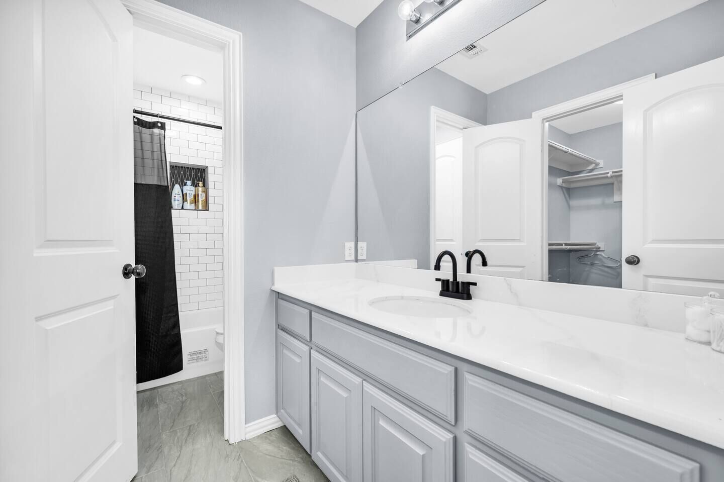 A modern bathroom with a white vanity, black faucet, and a large mirror.