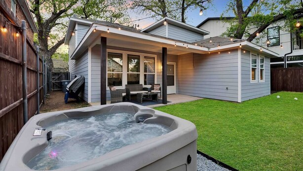 A backyard with a hot tub, a covered patio, and a lawn.