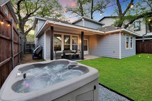A backyard with a hot tub, a covered patio, and a lawn.