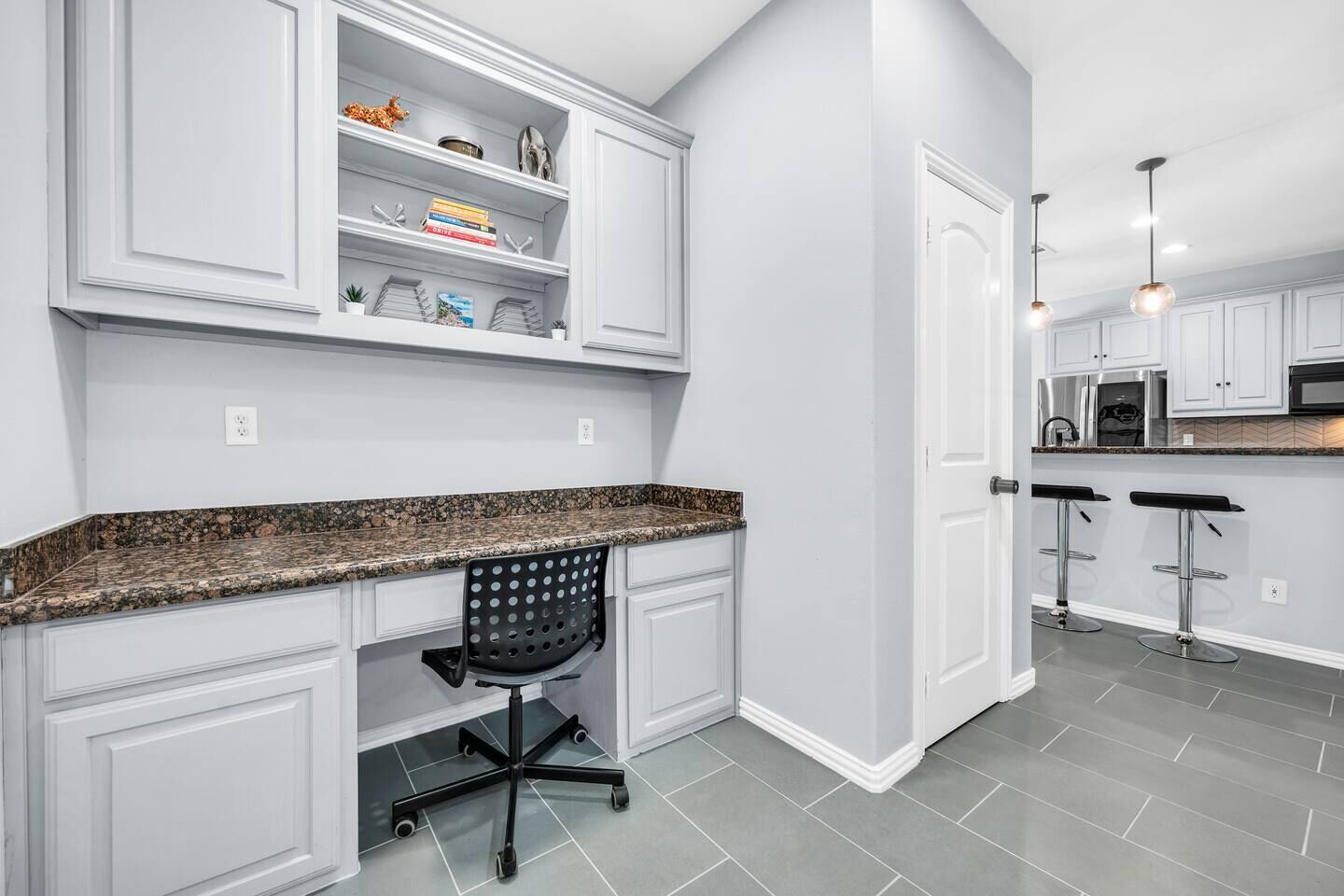 A modern kitchen with white cabinetry, granite countertops, and a black office chair.