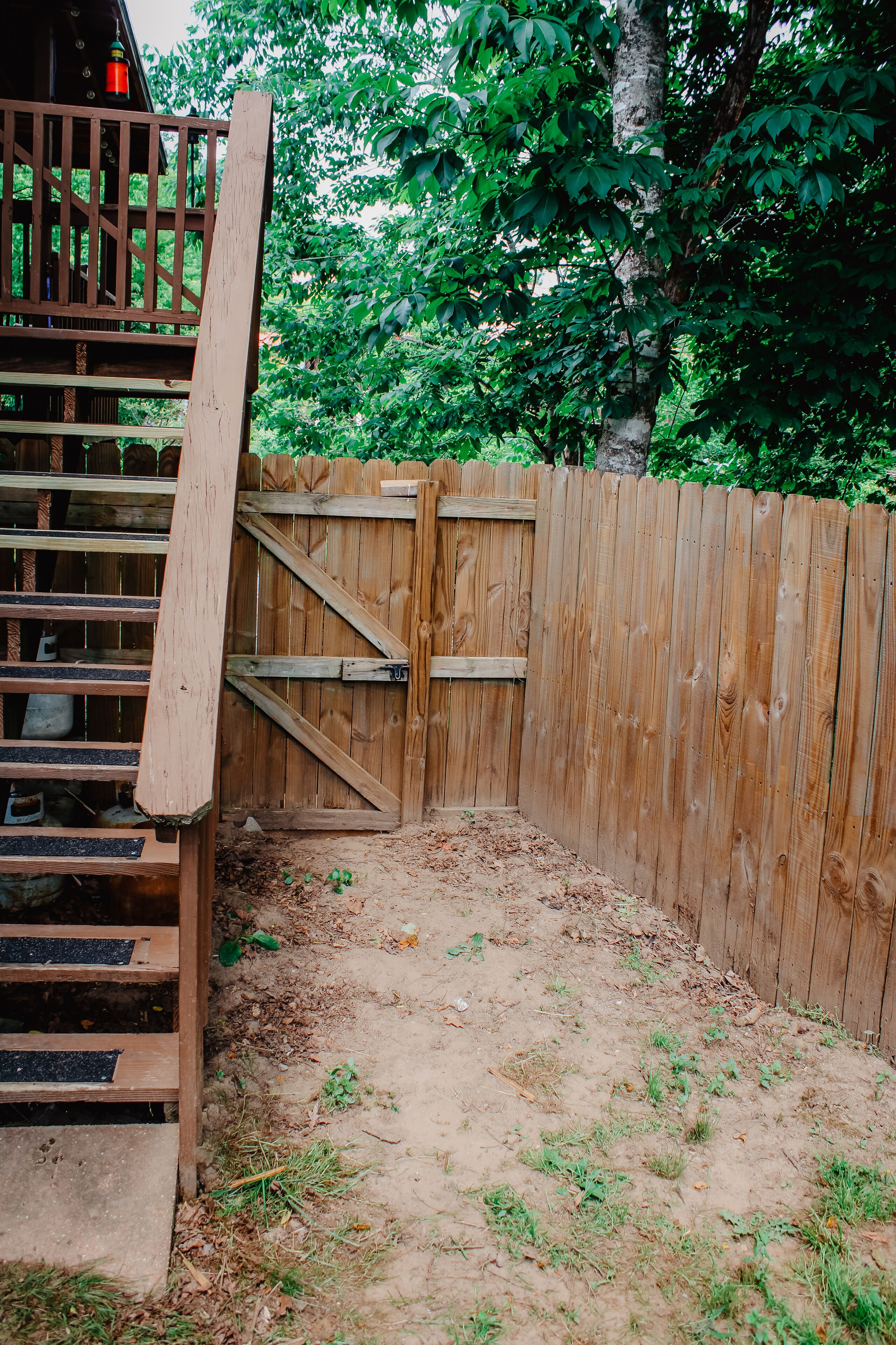 A wooden fence with a gate, a wooden staircase, and a dirt ground area.