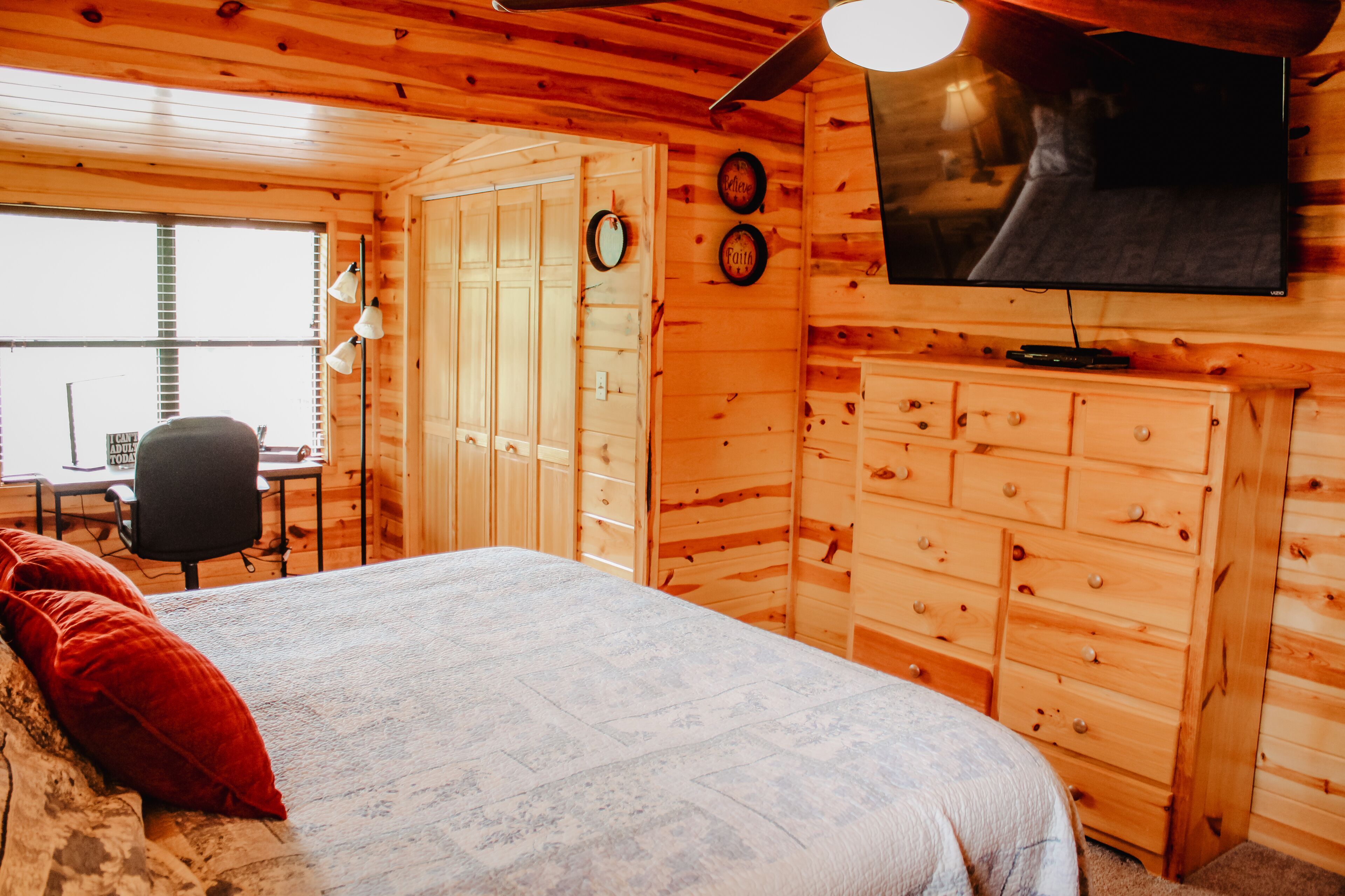 A wooden cabin room with a bed, a desk, and a TV mounted on the wall.