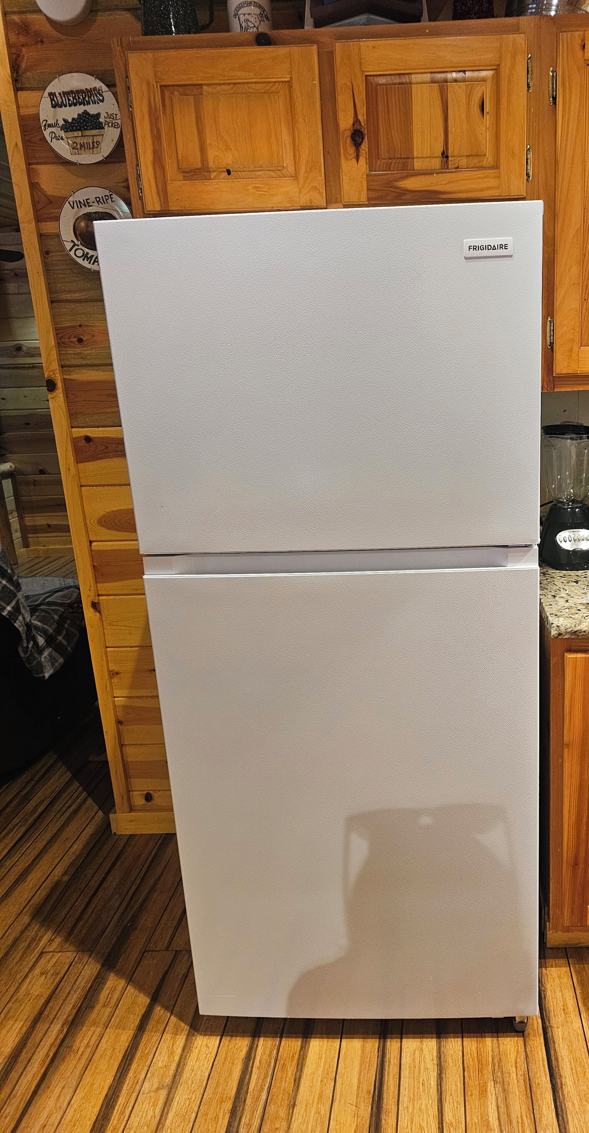A white double-door refrigerator in a kitchen with wooden cabinets and a wooden floor.