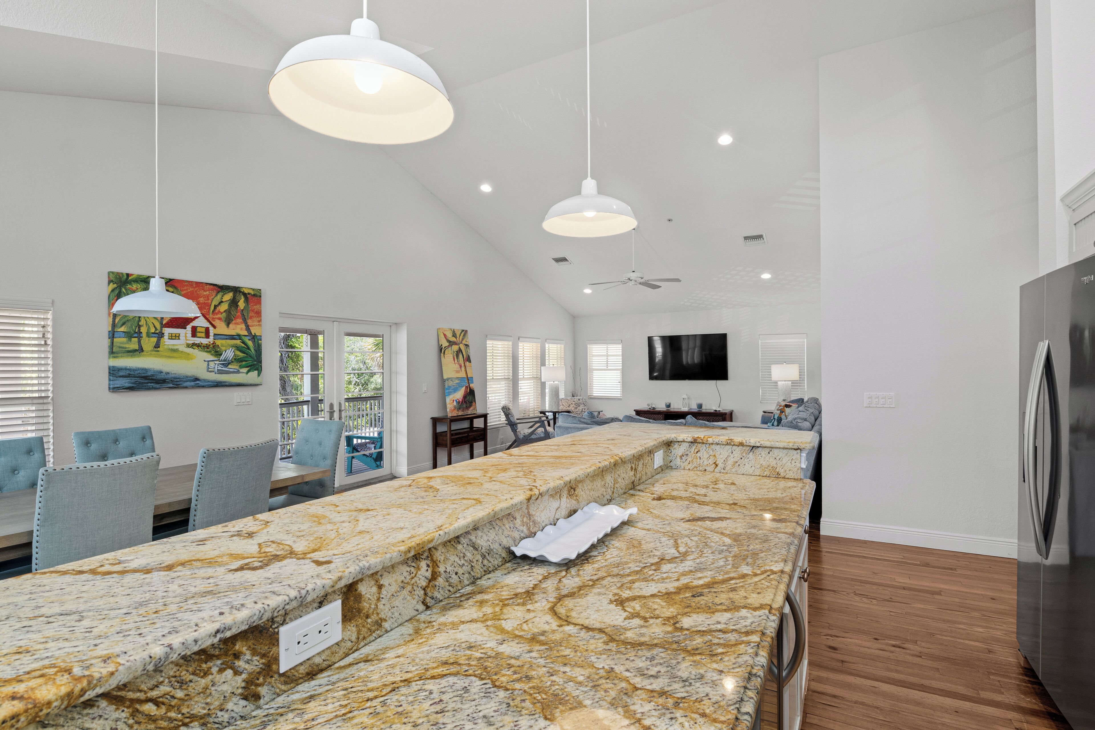 A spacious kitchen with a marble countertop, pendant lights, and a built-in refrigerator.