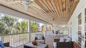 A covered outdoor area with wooden flooring, seating arrangements including a sofa and chairs, a table with a bowl, and a ceiling fan. - Anna Maria Guest House 401- 3 bedrooms in the middle of everything- 2 night mini (Anna Maria)