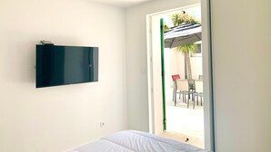 A bedroom with a bed, a mounted TV, and a door leading to an outdoor patio area with a table and chairs. - CAPUCINE (6 chemin des Biches, La Couarde) (La Couarde-sur-Mer)