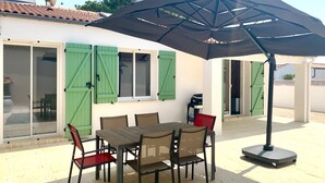 An outdoor patio with a table and chairs, a large umbrella, and a scooter. - CAPUCINE (6 chemin des Biches, La Couarde) (La Couarde-sur-Mer)