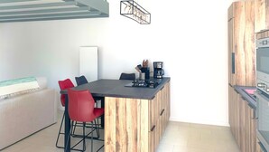 A modern kitchen with a central island, red chairs, a coffee machine, and a built-in oven. - CAPUCINE (6 chemin des Biches, La Couarde) (La Couarde-sur-Mer)