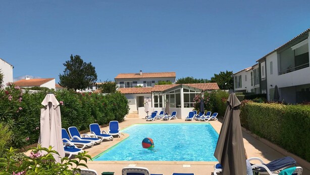A swimming pool with blue lounge chairs and umbrellas, surrounded by greenery and buildings. - Harmony, new apartment with heated pool (La Flotte)
