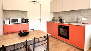 A compact kitchen with a wooden dining table, a black chair, and a red countertop. - Harmony, new apartment with heated pool (La Flotte)