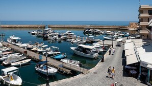 Un port de plaisance où sont amarrés différents types de bateaux, une promenade pavée et un bâtiment doté d’une terrasse.