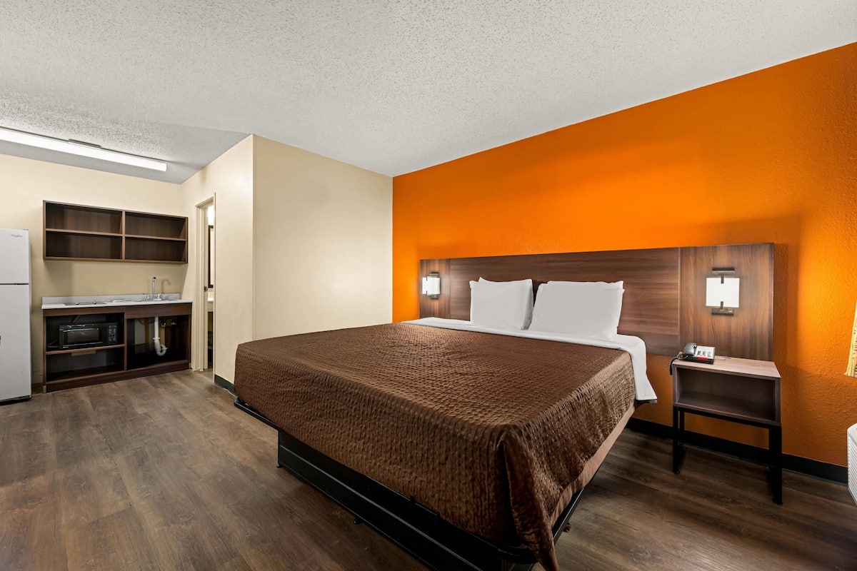 A hotel room with a bed, bedside table, and a kitchenette area.