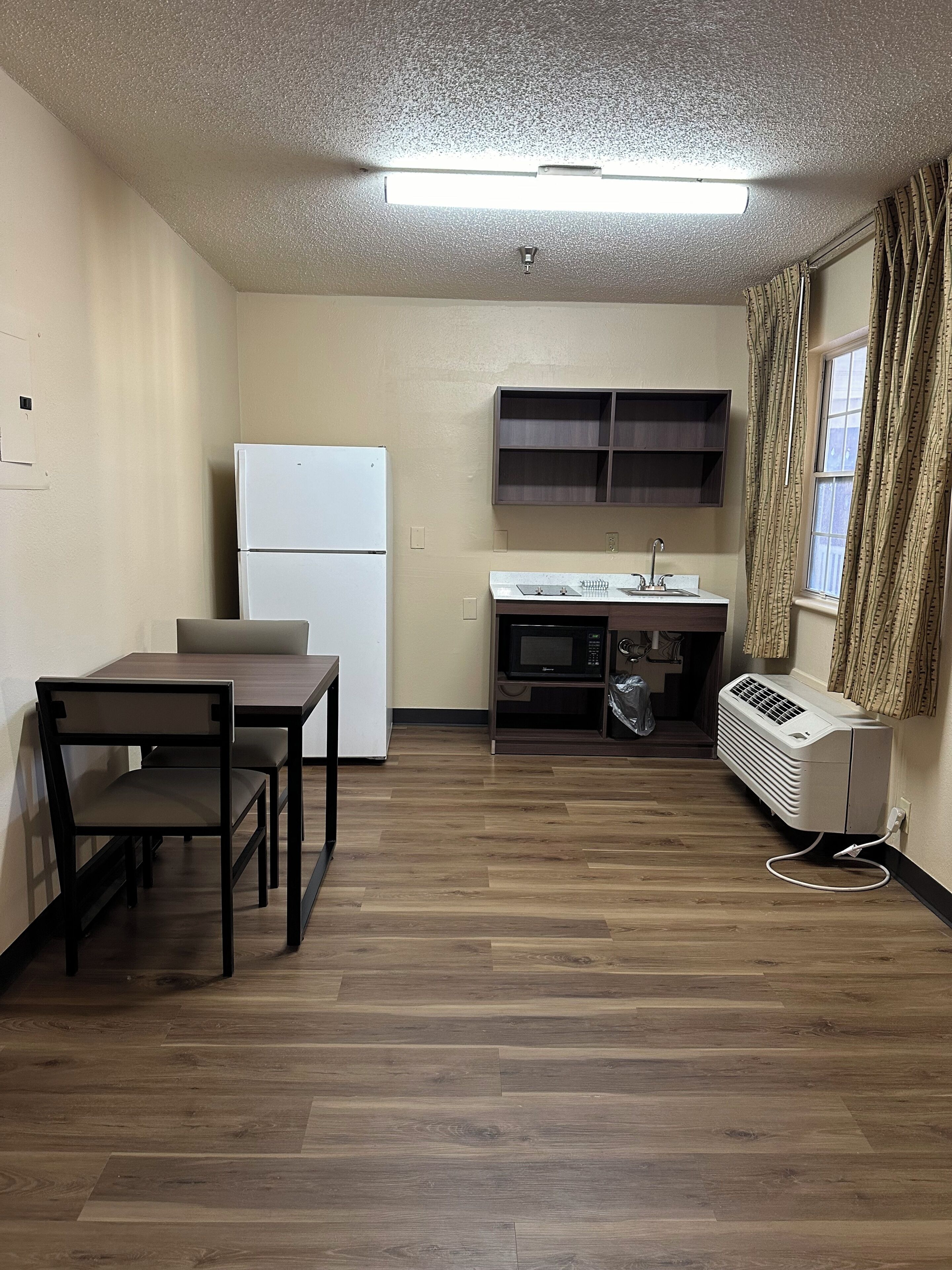 Una cocina compacta con refrigerador, microondas y estufa, una mesa de comedor con sillas, y un ventanal con cortinas.
