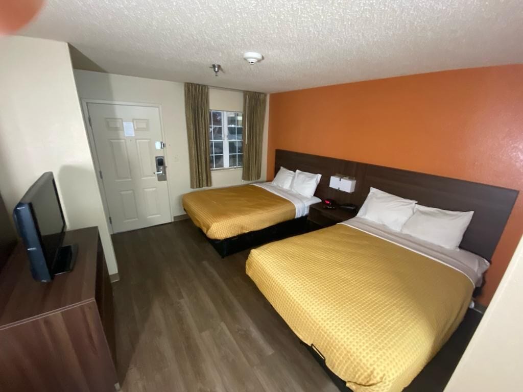 Habitación de hotel con dos camas, televisión, puerta y ventana con cortinas.