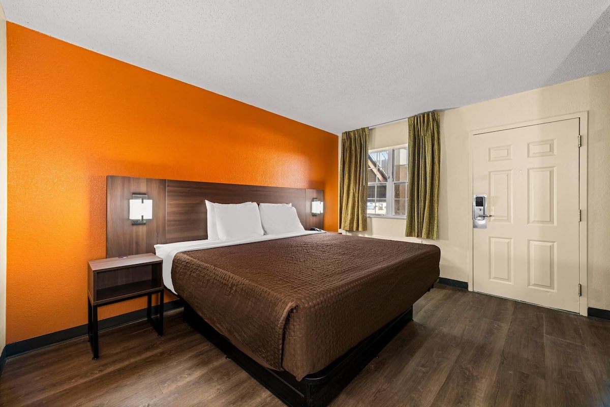 A hotel room with a large bed, a nightstand, a window with curtains, and a door.