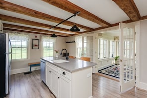 A kitchen with wooden beams, a large island, and a view of the outdoors.