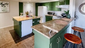 A modern kitchen with green cabinets, a granite countertop, and a central island with stools.