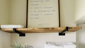A bathroom with wooden shelves holding towels and a framed quote on the wall.