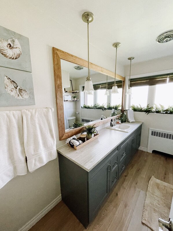A modern bathroom with a large mirror, two pendant lights, a sink, and a wooden vanity. - Short Drive to Point Pelee! Forget Your Worries in This Spacious & Serene Space (Leamington)