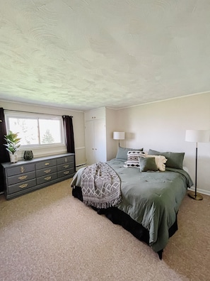 Un dormitorio con cama, cómoda, ventana y lámpara.