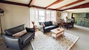 A living room with a black leather sofa, a wooden coffee table, and a patterned rug. There is a dining area with a table and chairs, and a kitchen in the background.