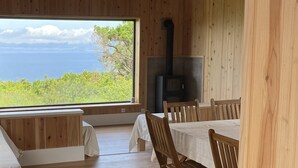 Un intérieur en bois avec une grande fenêtre, des poutres apparentes en bois au plafond et une cheminée.