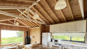 L’intérieur d’une cabane est doté d’un plafond en bois, de meubles blancs, d’un coin cuisine et d’une grande fenêtre donnant sur un paysage verdoyant.