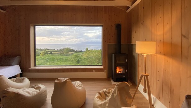 Une pièce chaleureuse avec une grande fenêtre, un poêle à bois et un lit offrant une vue agréable.