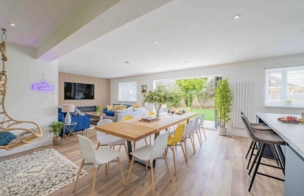 Un salon moderne avec une table à manger en bois, des chaises blanches et jaunes, un canapé bleu et un téléviseur.
