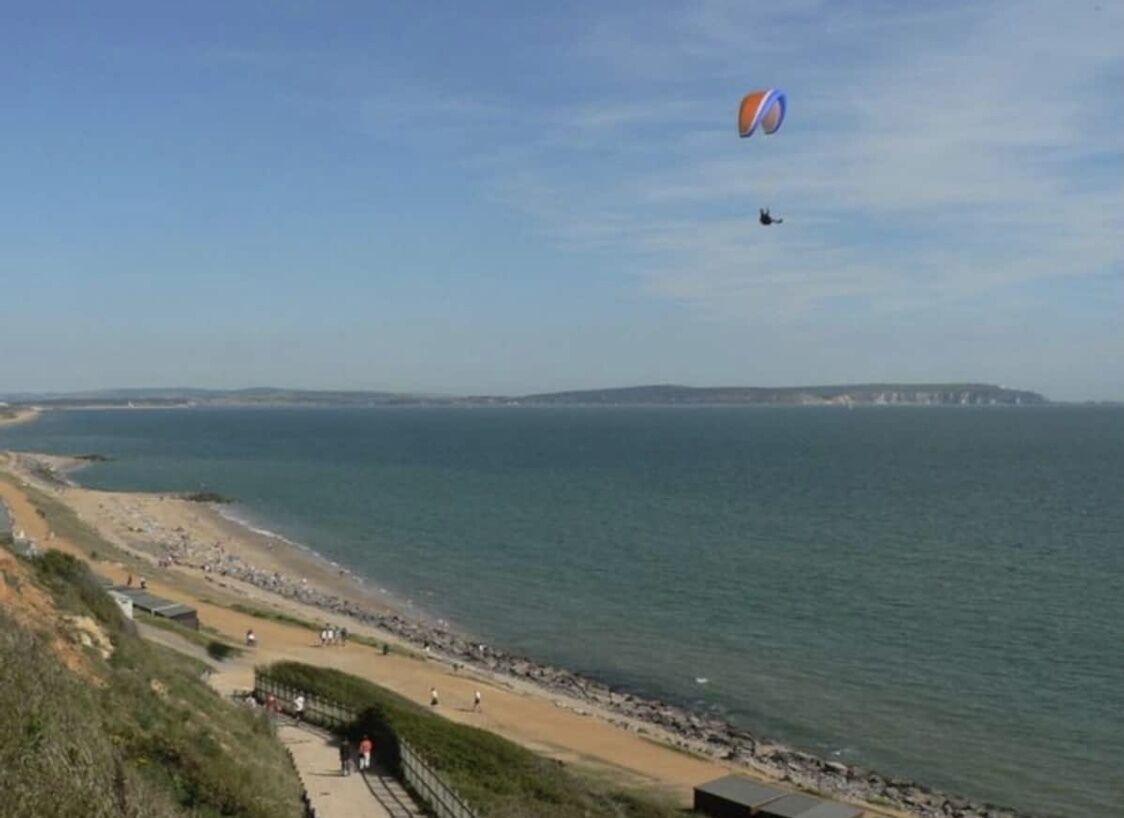A coastal beach with a clear sky, a kite, and a distant cityscape.