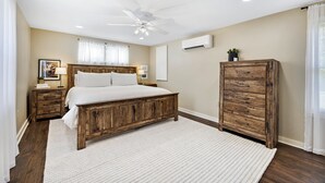Quarto com cama de madeira, mesa de cabeceira, guarda-roupa, ventilador de teto e aparelho de ar condicionado.