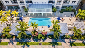 A rooftop pool area with lounge chairs, palm trees, and a clear blue pool.