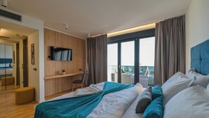 A modern hotel room with a large bed, a desk, a TV, and a balcony with a view. - Villa Luna- Private Heated Pool (Novalja)