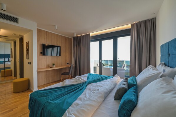 A modern hotel room with a large bed, a desk, a TV, and a balcony with a view. - Villa Luna- Private Heated Pool (Novalja)