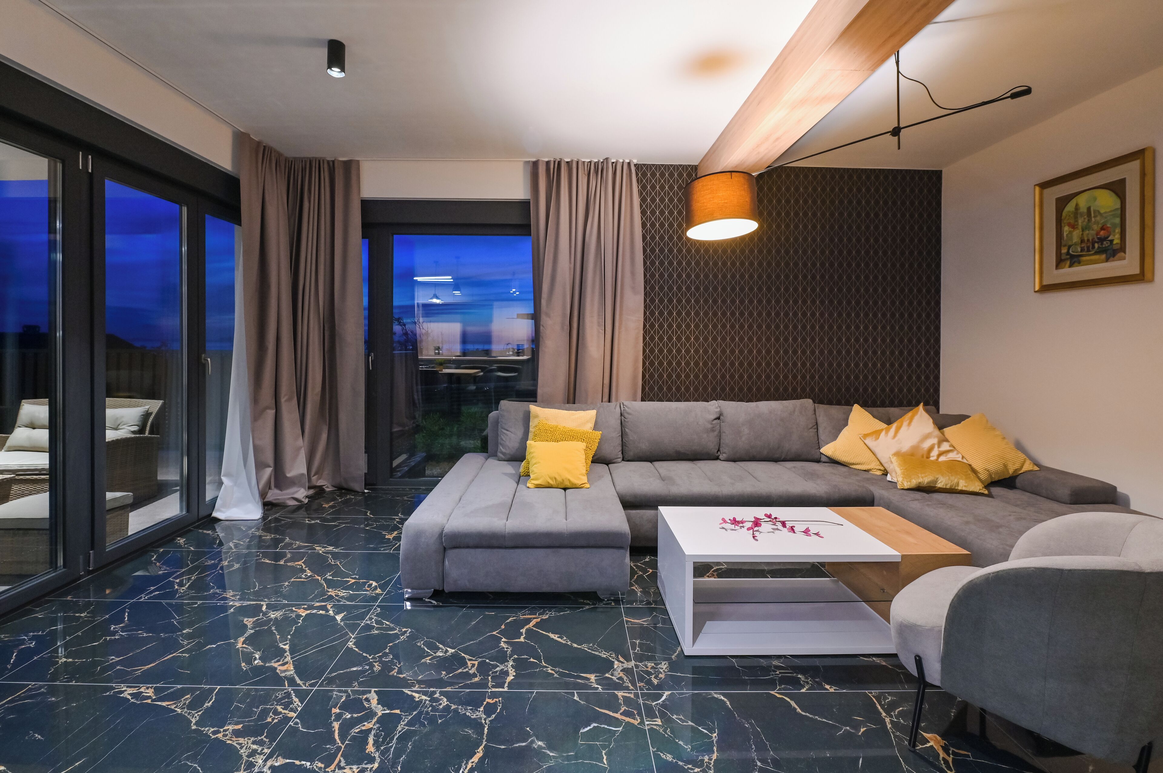 A modern living room with a sectional sofa, a coffee table, and a view through large glass doors.