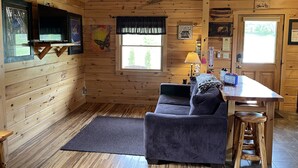 Ein Blockhaus-Interieur mit Holzwänden, einer Couch, einem Tisch und einem Fenster.