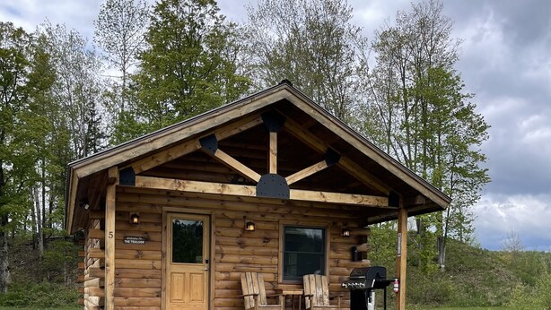 Eine Holzhütte mit Veranda, zwei Stühlen und einem Grill.