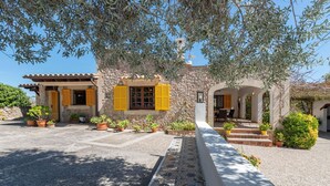 Un bâtiment en pierre avec des volets jaunes, des plantes en pot et un chemin dallé menant à l’entrée.