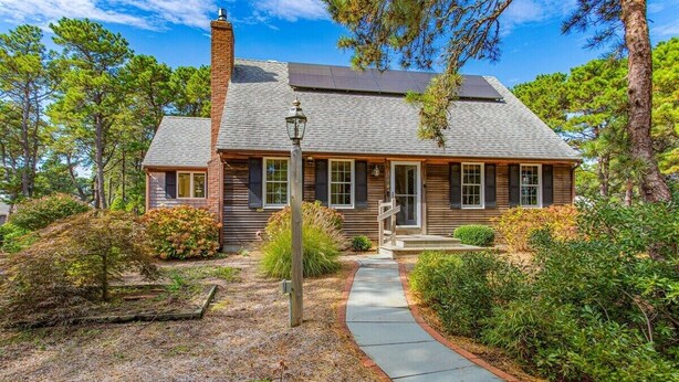 A two-story wooden house with a sloped roof, a front porch, and a pathway leading to the entrance. - Path to Herring Pond Beach (Eastham)