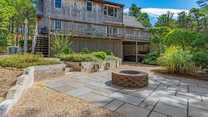 A two-story wooden house with a balcony, stone patio, and a fire pit. - Path to Herring Pond Beach (Eastham)