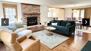 A living room with a brick fireplace, a green sofa, a beige sofa, and a coffee table. - Path to Herring Pond Beach (Eastham)