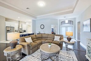 Ein modernes Wohnzimmer mit einer Eckcouch, zwei runden Tischen und einer Küche im Hintergrund.