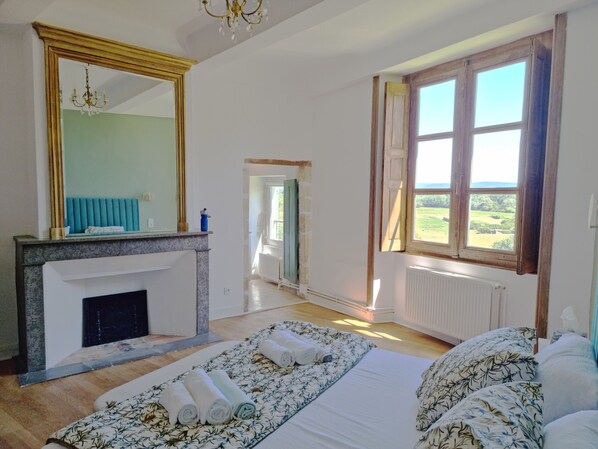 A bedroom with a large bed, a fireplace, a mirror, and a view of the outdoors.