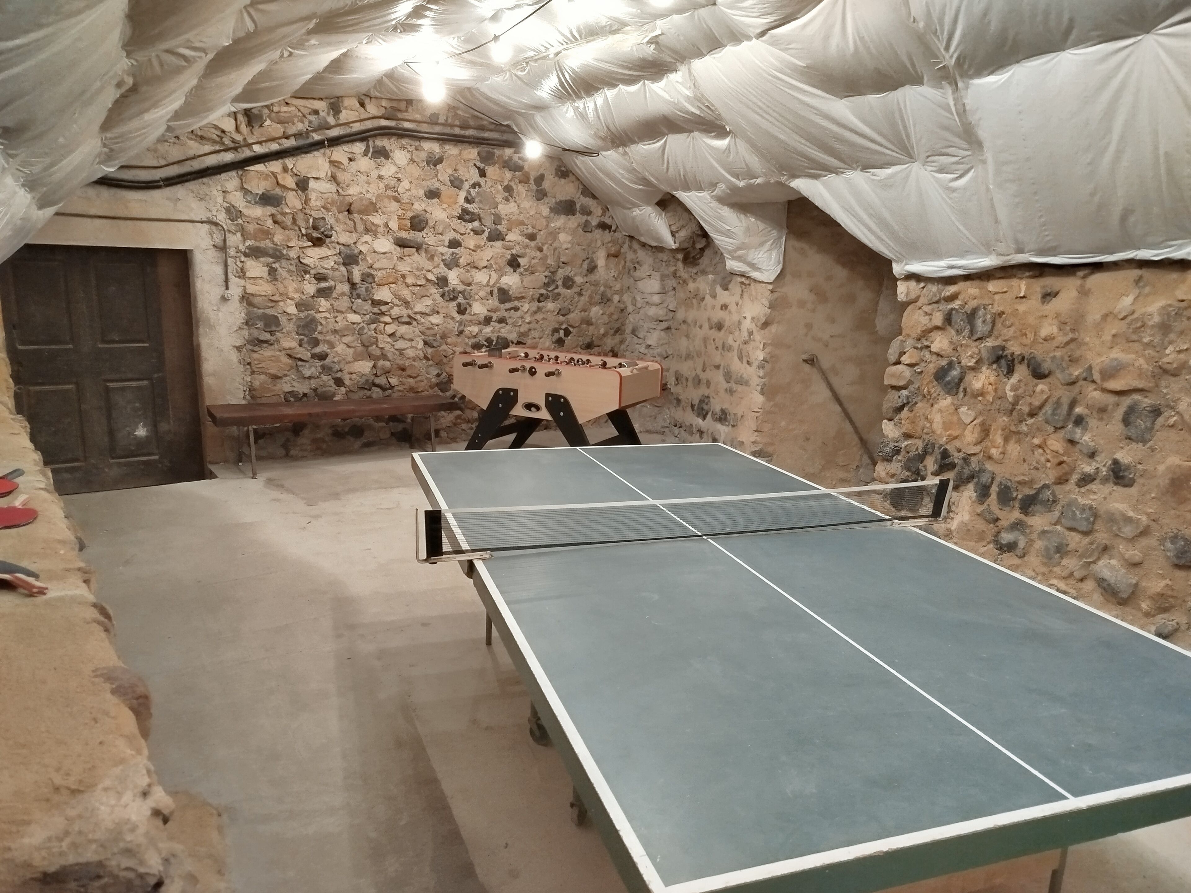 Une pièce équipée d’une table de ping-pong, d’un banc en bois et d’un baby-foot.