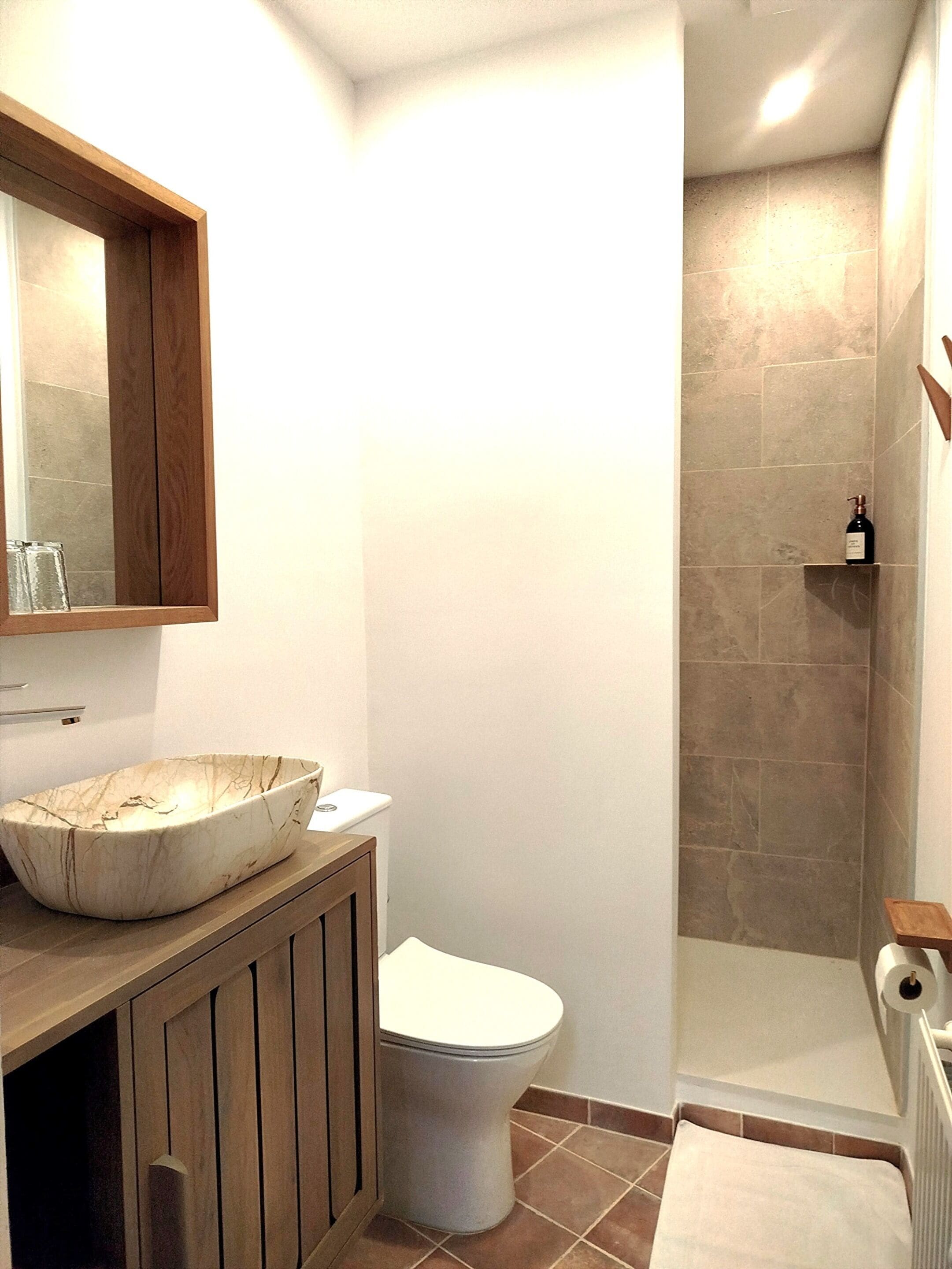 A bathroom with a marble sink, wooden vanity, white toilet, and a shower area with stone tiles.