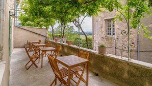 An outdoor patio with wooden tables and chairs, a stone wall, and potted plants.