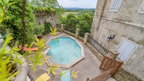 A wooden deck with a swimming pool, surrounded by greenery and a stone wall.
