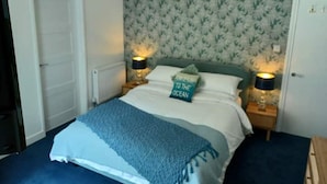 Et soveværelse med en seng, to sengeborde med lamper, et dekorativt vægophæng og en dør.